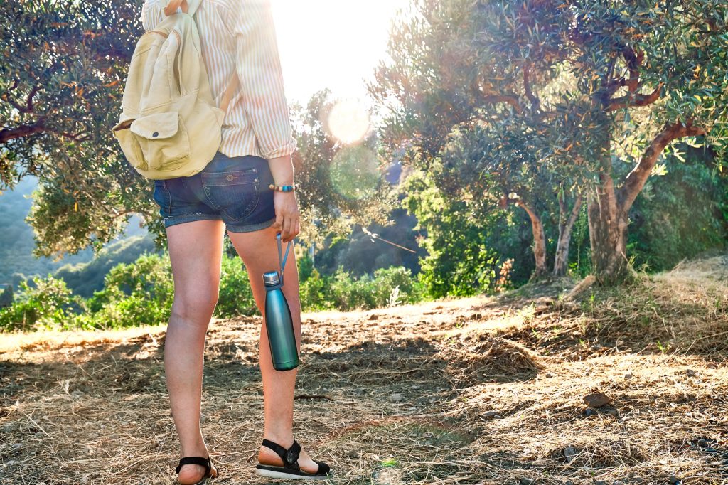 Woman walking in olive grove holding steel thermal bottle flask